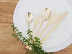 SALUSエレガンテシリーズの18-10ステンレスゴールド製スプーン、フォーク、プレートがテーブルに美しく並べられた食器セット