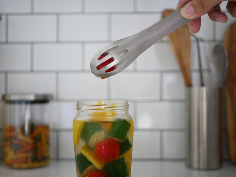 ステンレス製トングと野菜がキッチンカウンターに並ぶ