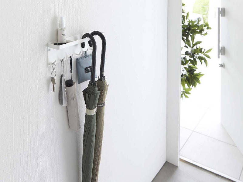 トレー付きスチール製アンブレラホルダー「tower」が石こうボードの壁に設置され、傘やバッグが掛けられている様子