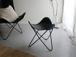 木製フロアのリビングルームに配置された、灰色のラップス製アイアンレザークラブチェア。快適なアームレスト付きでナチュラルな雰囲気を演出