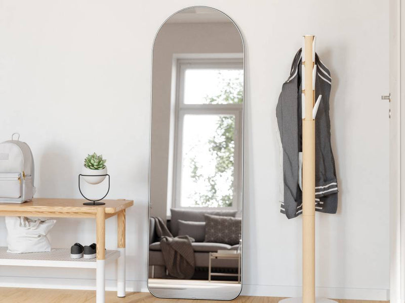 木製の床に置かれたフーバ アーチド リー二ングミラーと、その周囲に配置された椅子やランプ、植物が調和する室内インテリア。