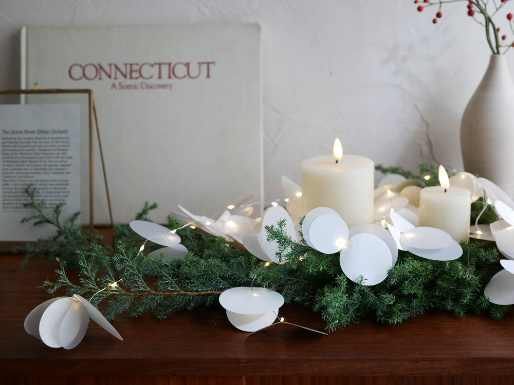 クリスマスのセンターピースとして飾られた紙製LEDキャンドル「Moon Light Tall」とキャンドルホルダー、常緑樹