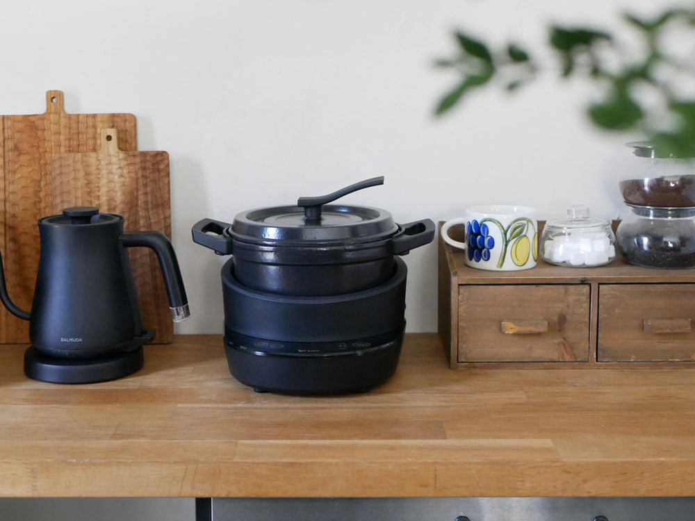 キッチンに置かれた水無し電気鍋「コツイラズ」と鍋セット。ポリプロピレン本体にフェノール樹脂の取っ手、鉄製のふたが特徴