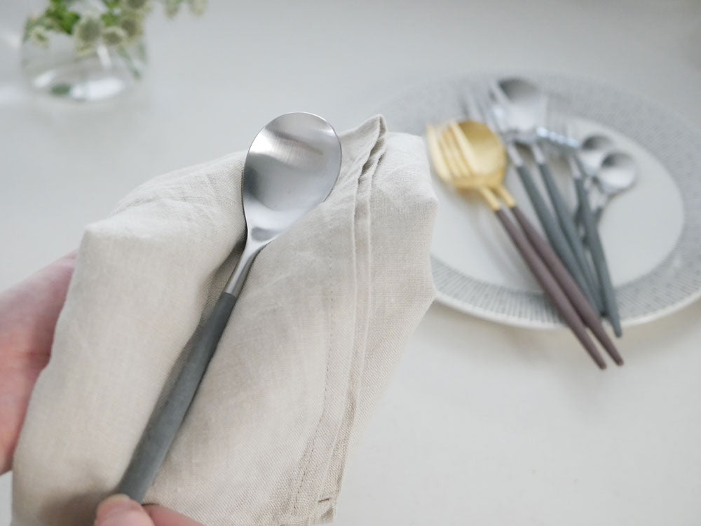 クチポールのMIOカトラリーセット(ブラウンゴールドとグレーシルバー)がテーブルクロスとナプキンと共に整然と並べられた様子。フォーク、スプーン、ナイフなどの食器が美しく配置されています。