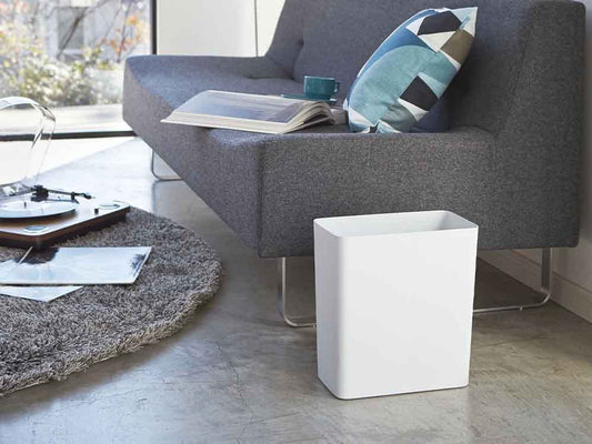 YAMAZAKI/towerのスチール製10リットルトラッシュカンがリビングルームの木製フローリング上に配置され、ソファやカーペット、植物と調和したインテリア