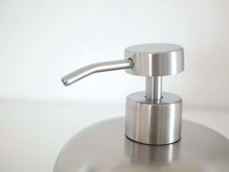 シルバーのステンレスソープディスペンサーと観葉植物、ランプ