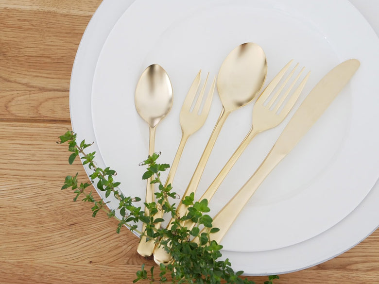 SALUSエレガンテシリーズの18-10ステンレスゴールド製スプーン、フォーク、プレートがテーブルに美しく並べられた食器セット