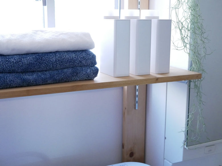 ブランドtowerの詰め替え用ランドリーボトルが木製の棚に並べられ、タオルや植物など家庭用品と共に配置されている様子