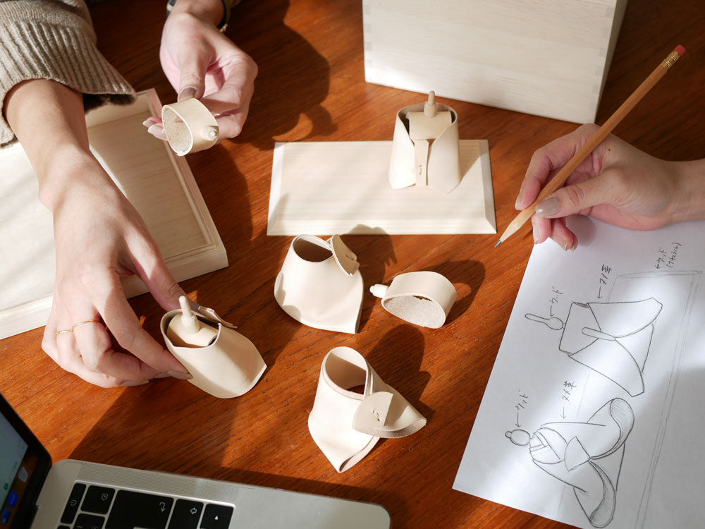 「Comore Sun」のヌメ革着物を纏ったお内裏様とお雛様が、ヒノキ製の台座に並んで飾られているお雛様セット