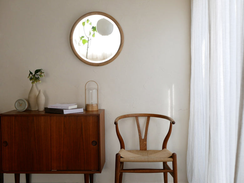 NOWHERE LIKE HOMEのブラウン無垢材フレームラウンドミラーが、木製床と調和した室内に設置されている様子