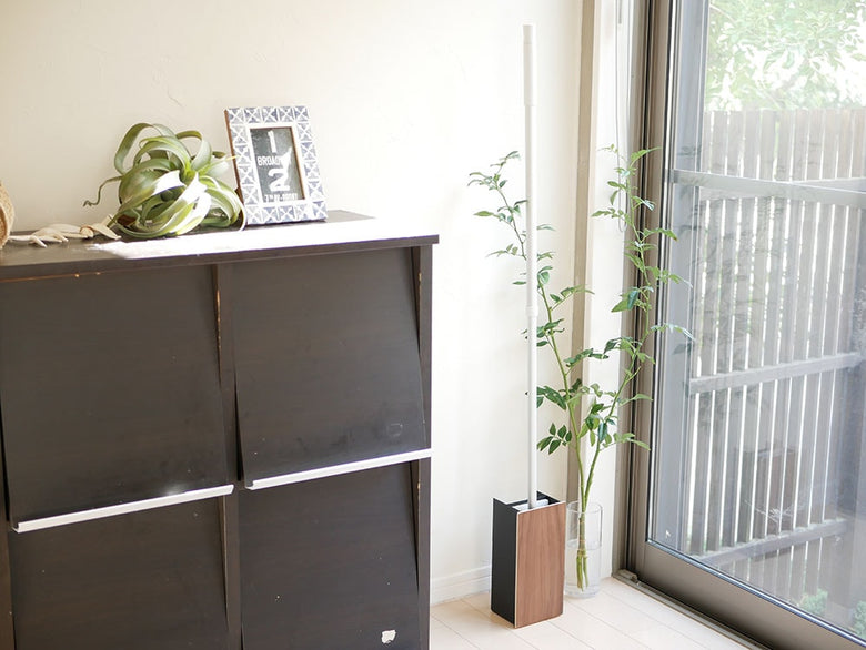 山崎の【RIN/リン】フローリングワイパースタンドが木目調の床とグレーのシェルビング、観葉植物と共にモダンな室内に配置されている様子