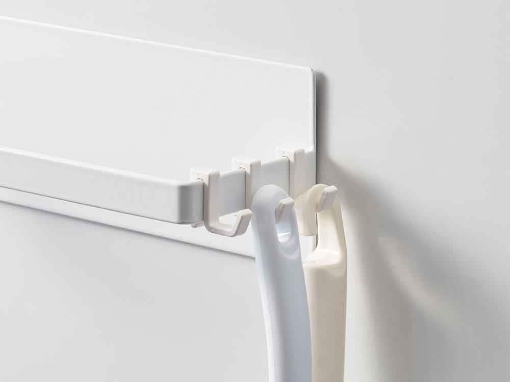 YAMAZAKI/towerの2段マグネット洗濯ハンガー収納ラックがスチール製の平らな壁面に取り付けられ、複数のハンガーが掛かっている様子