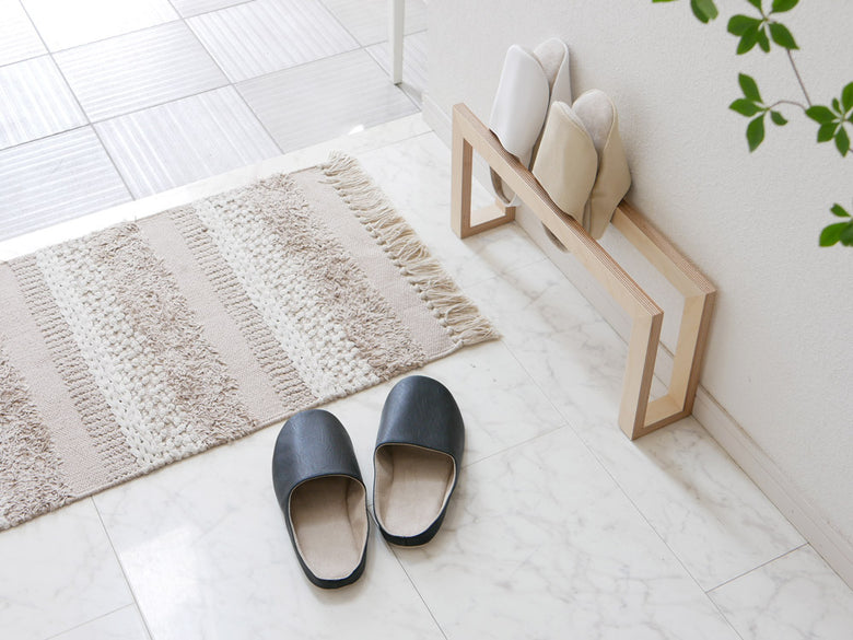 リビングルームの木製床とカーペットの上に置かれた【sarasa design/サラサデザイン】b2c プレーンステッチ ルームシューズ