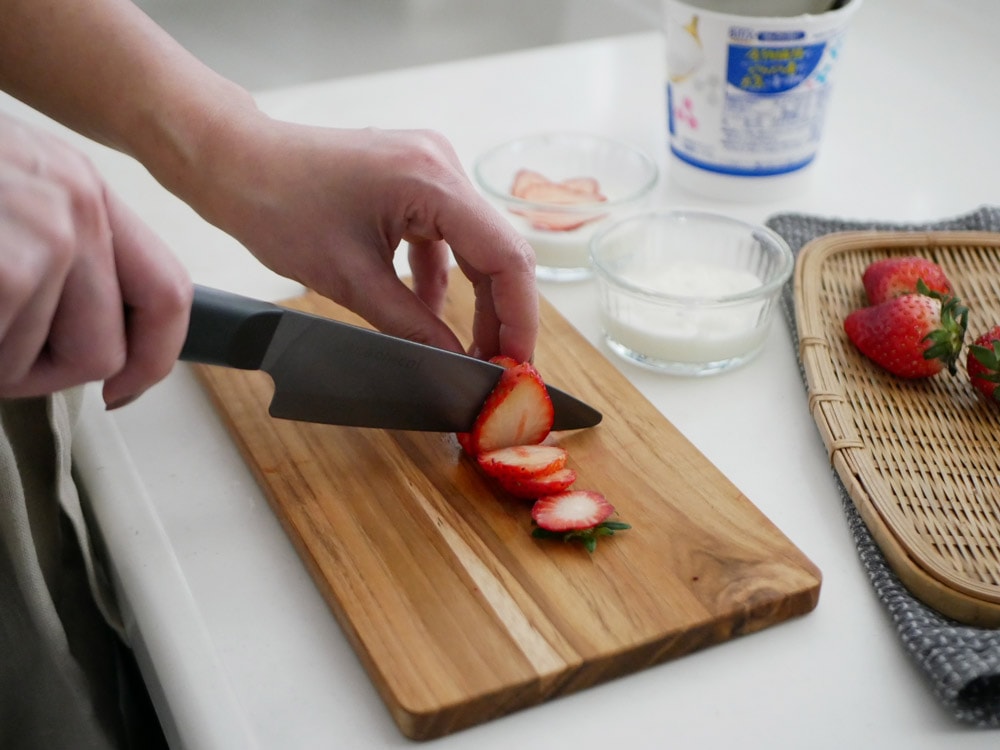 京セラココチカルのセラミックキッチンナイフが木製まな板の上に並べられ、新鮮な野菜と果物が周囲に配置された調理準備の様子