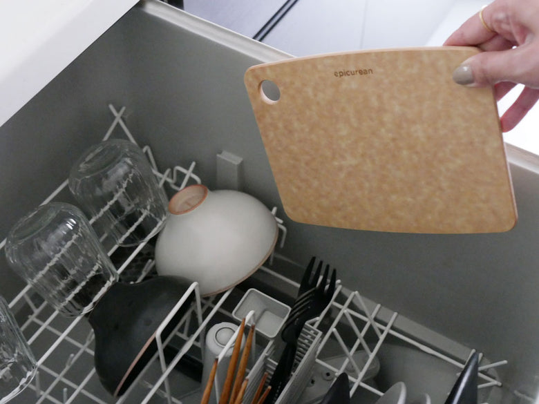 エピキュリアン製セルロース繊維カッティングボードがキッチンカウンタートップに置かれ、銀色の食器や家庭用調理器具、食器乾燥ラックが周囲に配置されています。