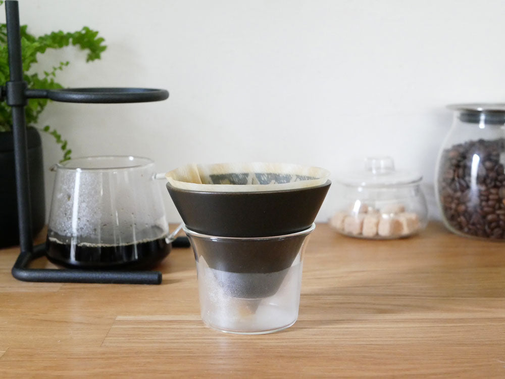 KINTOのブラックブリュワースタンドセット。ステンレス製スタンドに耐熱ガラスのサーバーとホルダー、磁器のブリューワー、コットンペーパーフィルターが整然と配置されています。