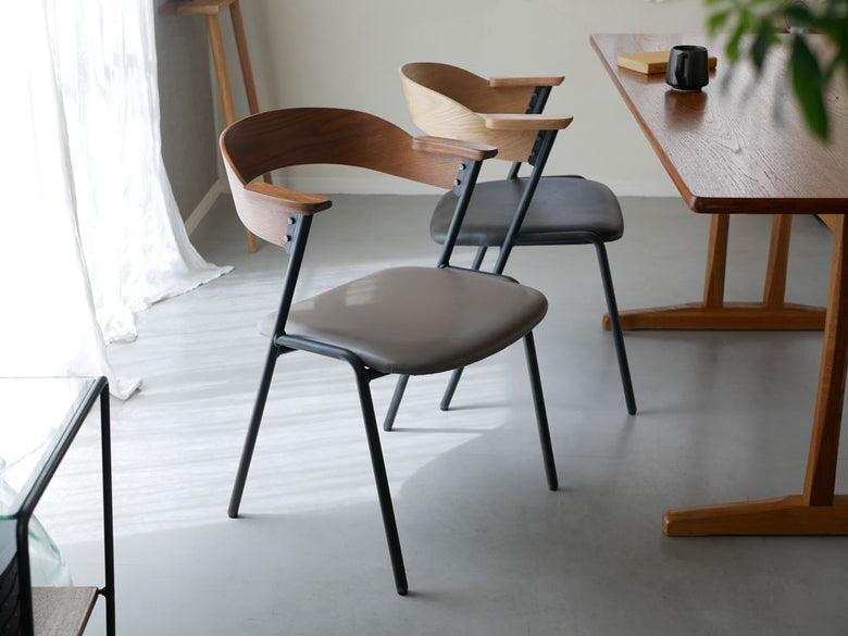 アデペシュのダニス ショートアームチェア。オーク突板とアッシュ無垢材を使用した木製フレームにPU座面を備え、木の床の上に配置されたスタイリッシュな椅子。