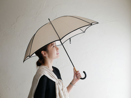 ビコーズのプレーンパイピング傘を持つモデルが晴天の中でポーズをとっている写真