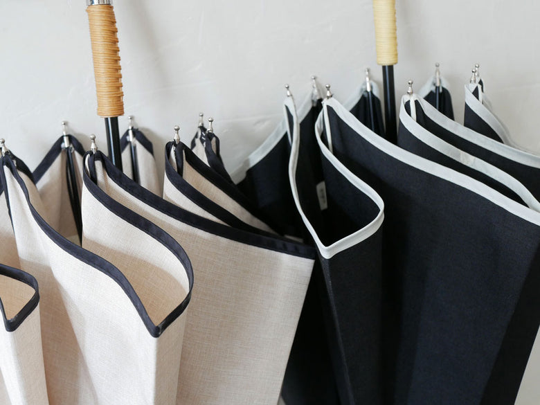 シルバーのハンガーに掛けられたビコーズのプレーンパイピング傘。ポリエステル100％の防水布地が特徴です。