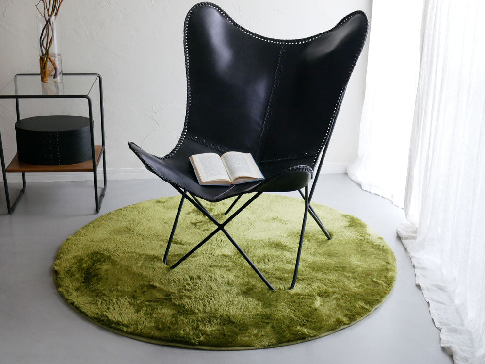 木製フローリングにグレーの【HOPPL/ホップル】円形ラグ130cmが敷かれ、椅子とクッションが配置された快適なリビングルーム