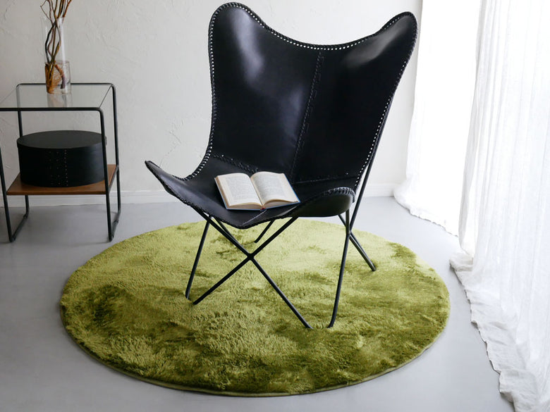 木製フローリングにグレーの【HOPPL/ホップル】円形ラグ130cmが敷かれ、椅子とクッションが配置された快適なリビングルーム