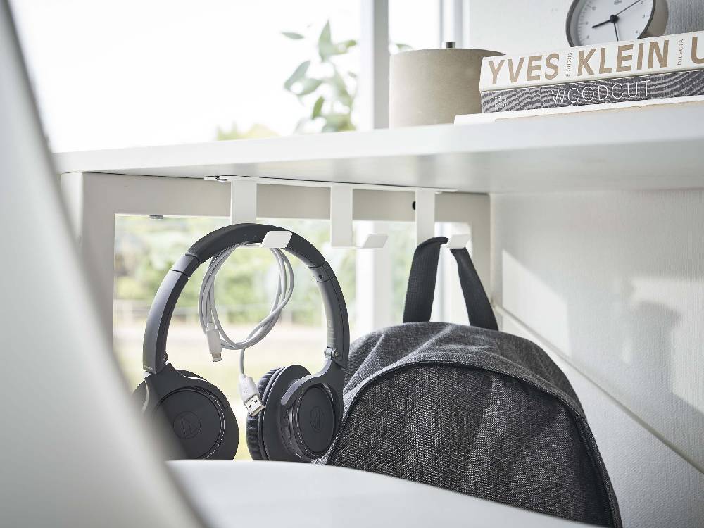 デスク下に取り付けられたスチール製の3連フックにヘッドフォンや電気ケーブルが掛かっている様子の画像