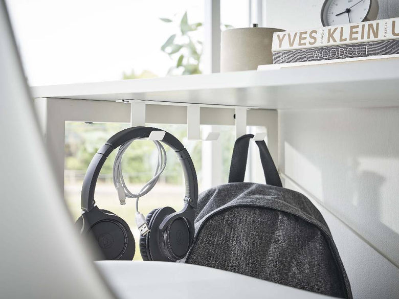 デスク下に取り付けられたスチール製の3連フックにヘッドフォンや電気ケーブルが掛かっている様子の画像