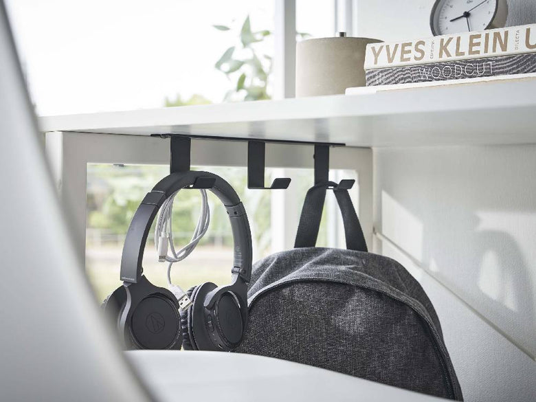 銀色のスチール製タワー型デスク下フック3連がデスク下に取り付けられ、ヘッドホンや電気ケーブルを整理している様子