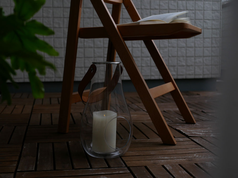 ホルムガード DESIGN WITH LIGHT ランタンが木製の床と家具、ガラス製の花鉢とともに配置されたスタイリッシュな静物写真