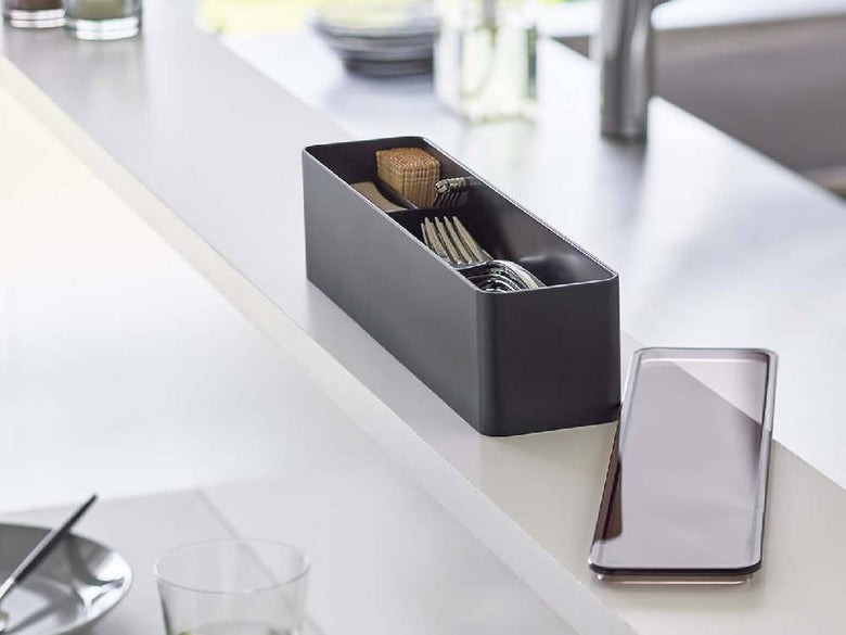 銀色の蓋付きカトラリーケースがキッチンカウンター上に置かれ、花鉢やキッチン用品とともにディスプレイされている