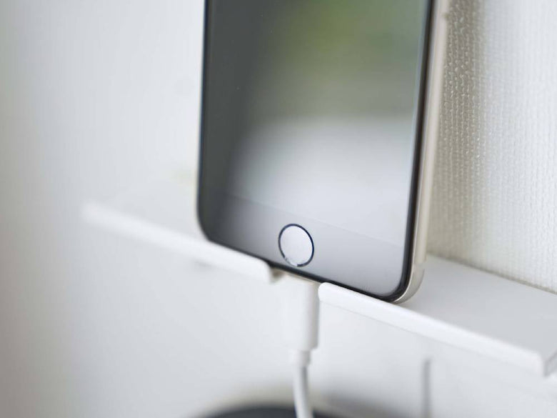 壁に取り付けられたスチール製のスマートフォン＆ヘッドホンホルダーに、スマートフォンとヘッドホンが掛けられている様子