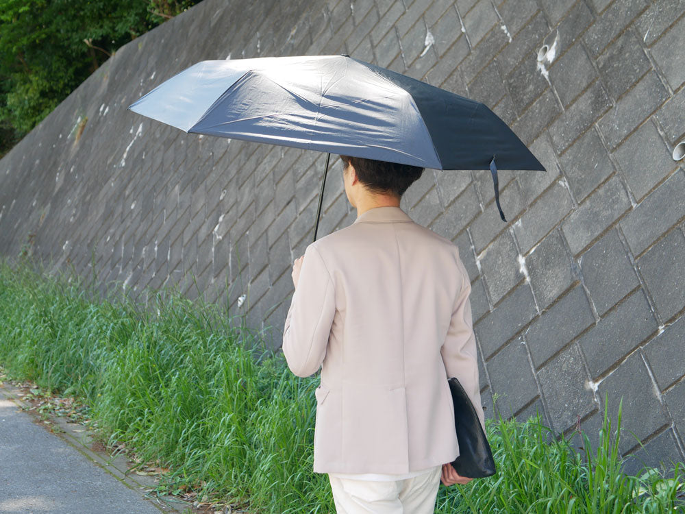 灰色のマブワイドライト遮光ミニ65傘をさして雨と風の中を歩く人
