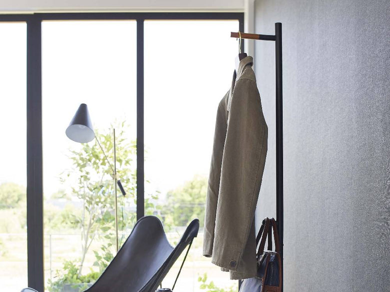 スチールと天然木製のタワーハンガーが木製の床と植物と共にエントランスに配置されている様子