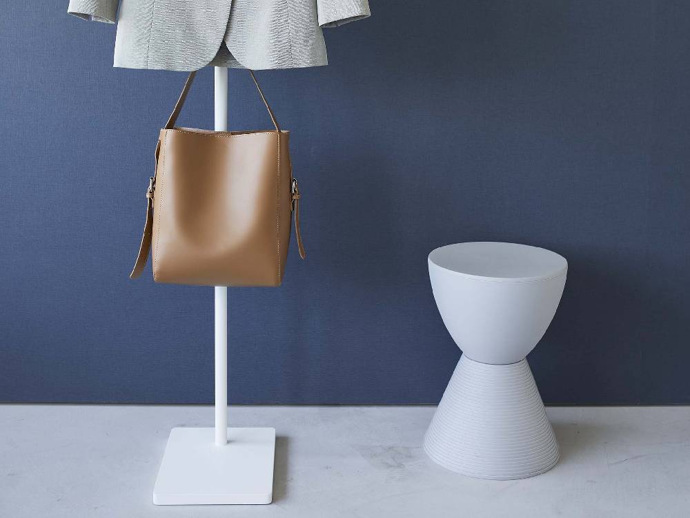 エントランスに設置されたスチールと天然木製のタワーハンガー。木製フロアの上に置かれ、陶器の花瓶と観葉植物が周囲に配置されています。