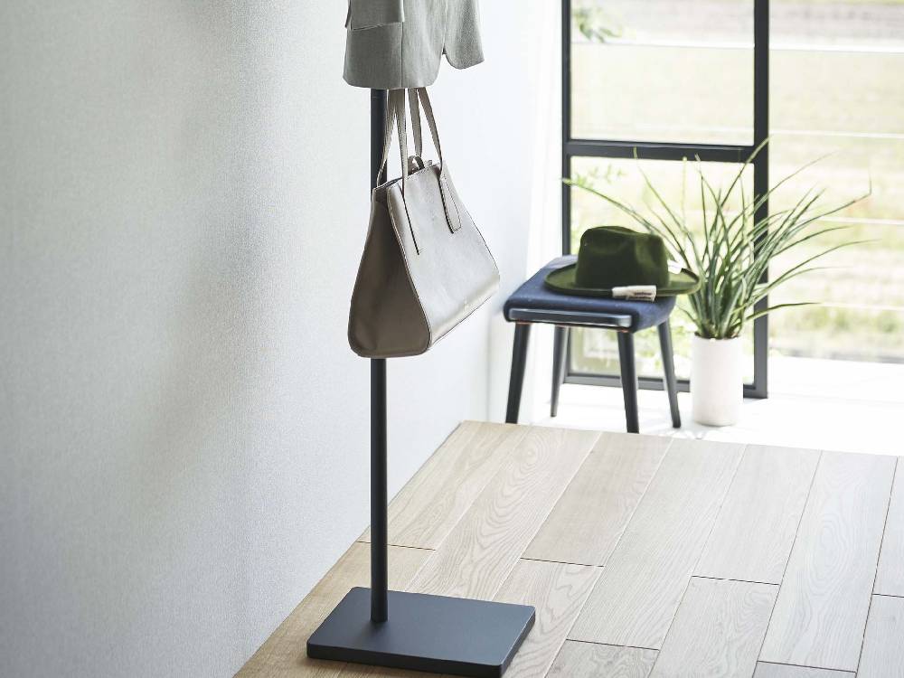 スチール製タワータイプのエントランスコートハンガーにバッグ、観葉植物、ランプが掛かっている様子