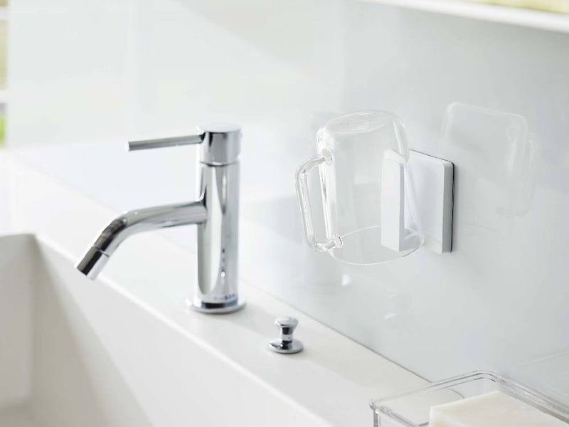 浴室の洗面台に取り付けられたミストブランドのフィルムフック タンブラーホルダーと、周囲の水栓やバスルームキャビネット、観葉植物が映し出されています。