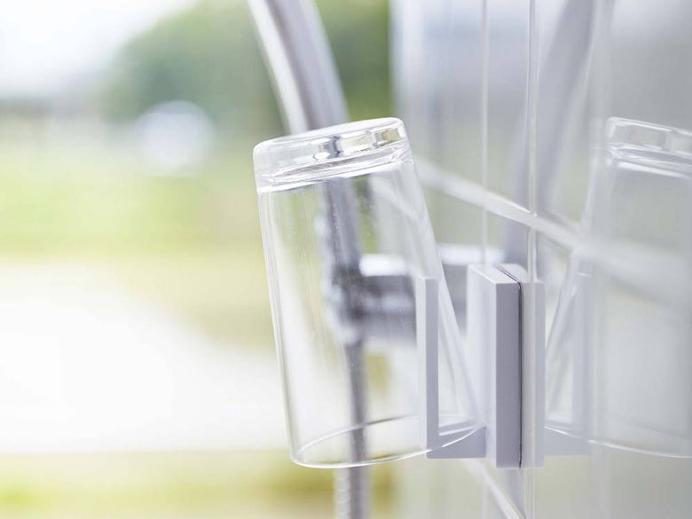 銀色と透明なプラスチック製フィルムフック タンブラーホルダーがガラスの壁面に取り付けられている様子