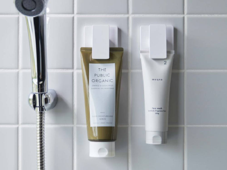 ワイドクリップ付きフィルムフックがバスルームの光沢ある壁面に取り付けられ、化粧品ボトルやヘアケア用品を掛けている様子