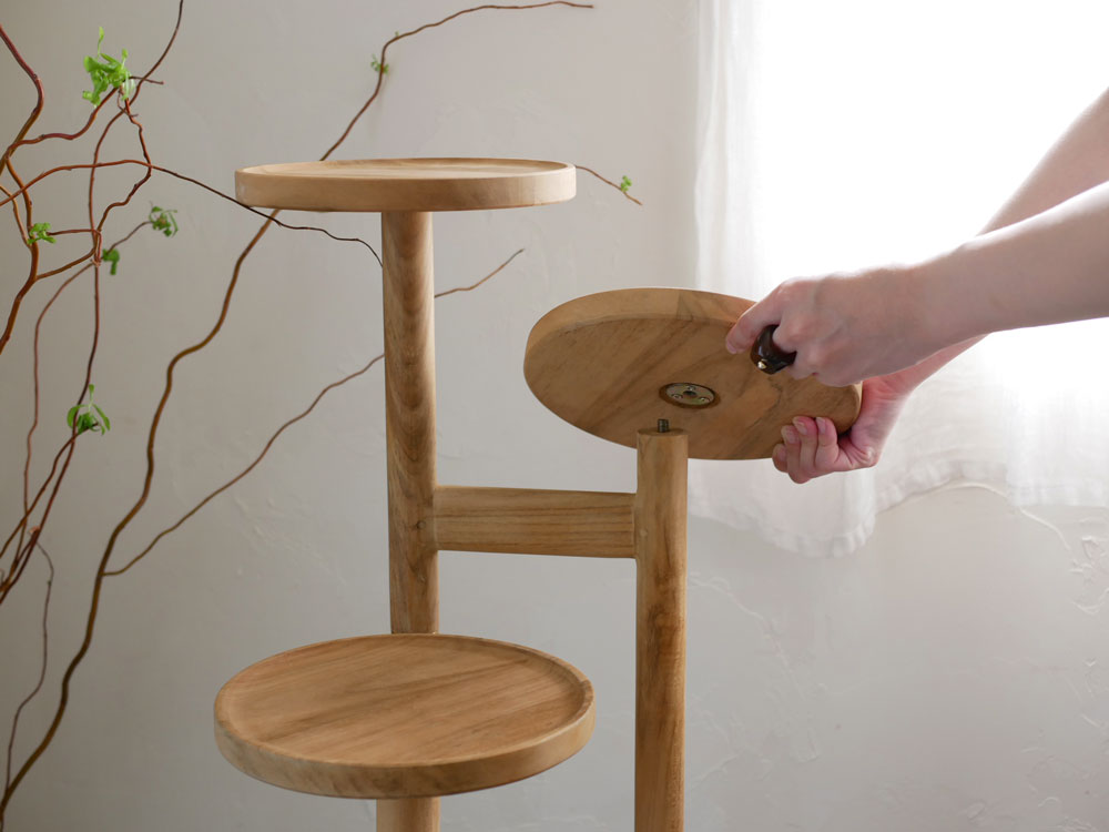 ナチュラル仕上げのチーク無垢材を使用したサンフラワーラタンのステップトレイテーブル。高さ100cmで3段の丸いトレイが配置された木製デザイン