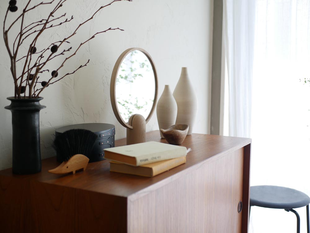 フリッツ・ハンセンのSkagerak Ainoミラーがハードウッドのリビングルームに配置され、照明や観葉植物、花瓶とともに上品なインテリアを演出している様子