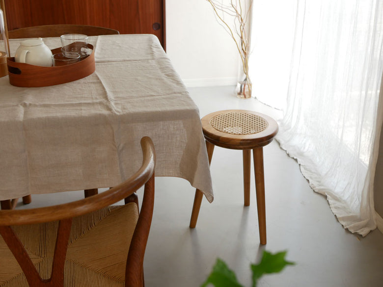 チーク材とラタン素材のサンフラワーラタンスツールが木製テーブルと椅子とともにハードウッドの床上に配置されている