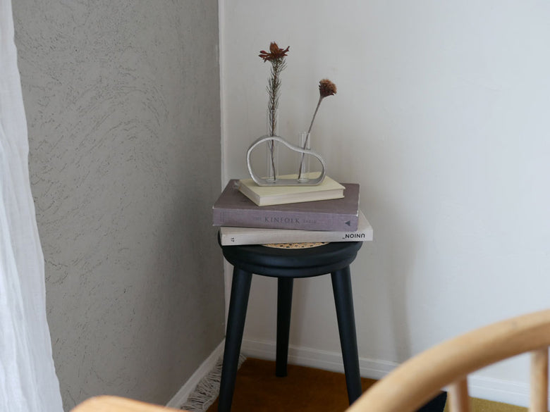 木製のエンドテーブル上に配置されたクレエのアルミガラスベースと花瓶、背景に木床とリネンがある室内の様子