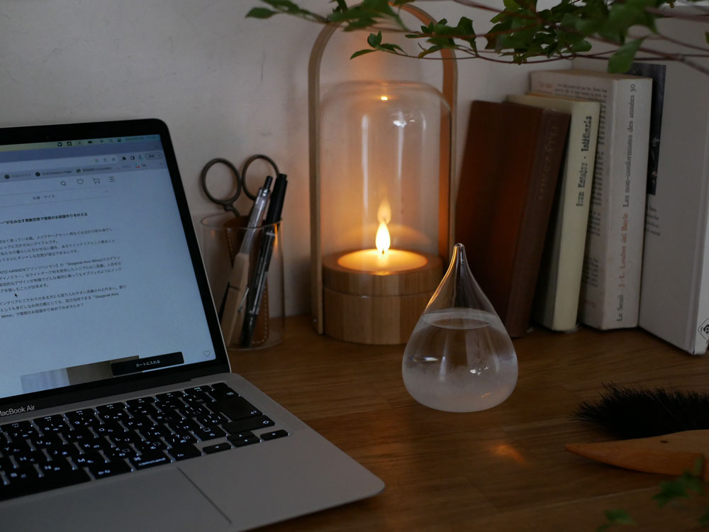 ガラス製のシリンダー型キャンドルランプが炎を灯し、木製ベースと観葉植物が配置されたオフィス用の静物写真