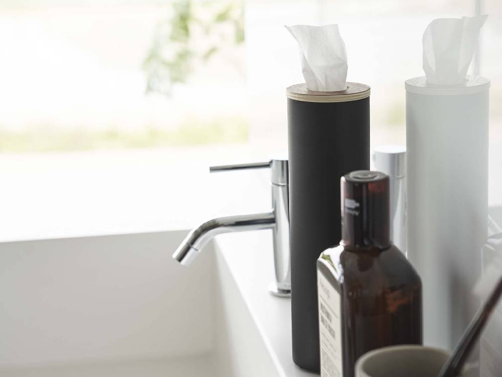 洗面台の上にスチールと天然木で作られた【RIN/リン】ボトル型ティッシュケース Sが置かれ、ソープディスペンサーやペーパータオルブラシなどのバス用品と共に整然と配置されている様子