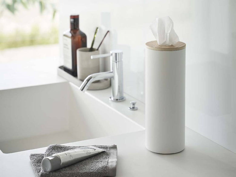 スチール製のボトル型ティッシュケースが洗面台の上に置かれ、蛇口やシンク、タオル、観葉植物などが一緒に配置されたバスルームの様子