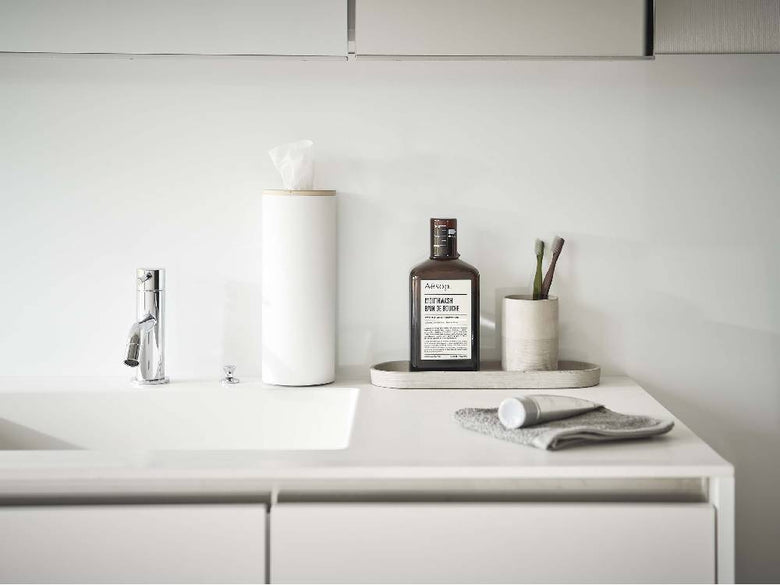 スチールと天然木のボトル型ティッシュケースがセラミックシンクと銀色の蛇口が配置されたカウンタートップに置かれたバスルームインテリア