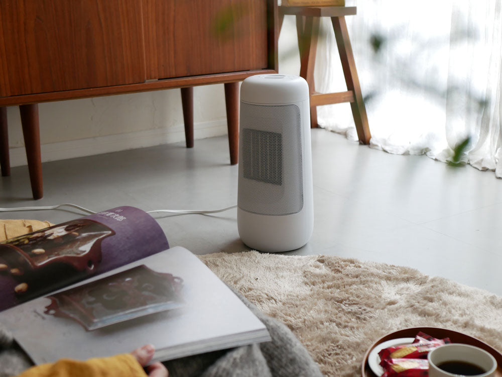 木製フローリングのリビングルームに設置されたハンドル付き首振りセラミックファンヒーターと観葉植物