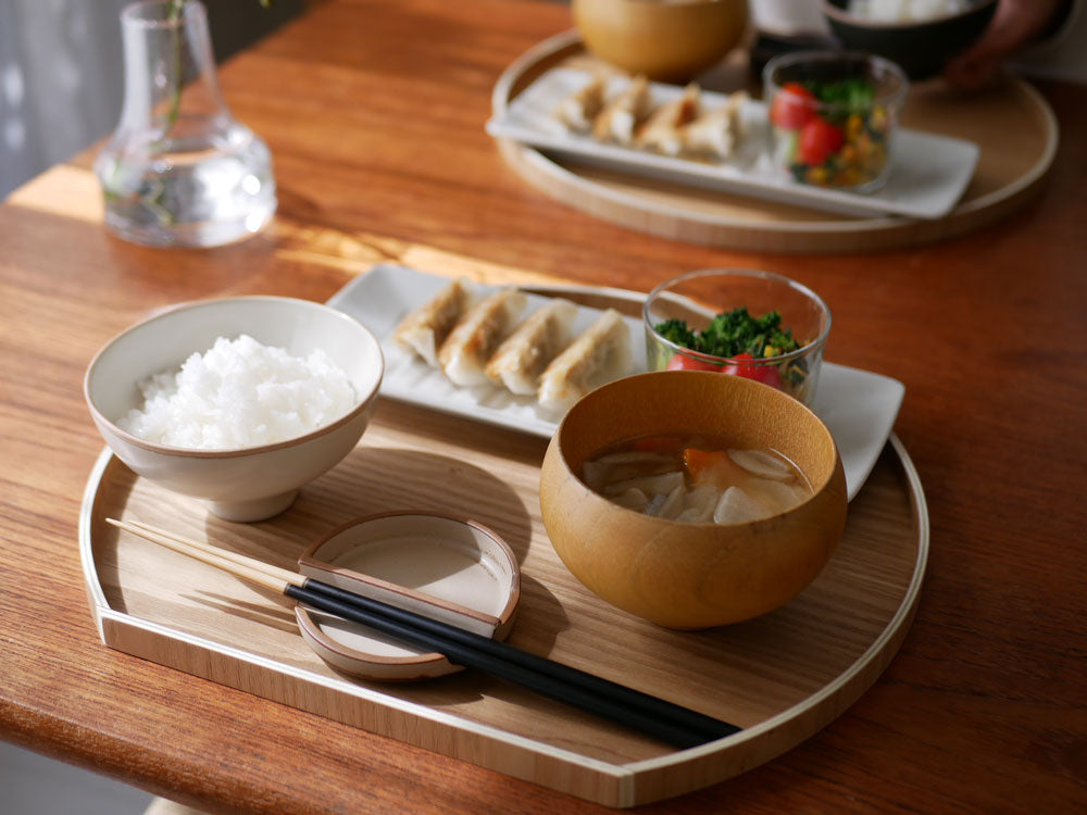 天然木の半月盆に盛り付けられた料理と箸がテーブルの上に配置されている様子