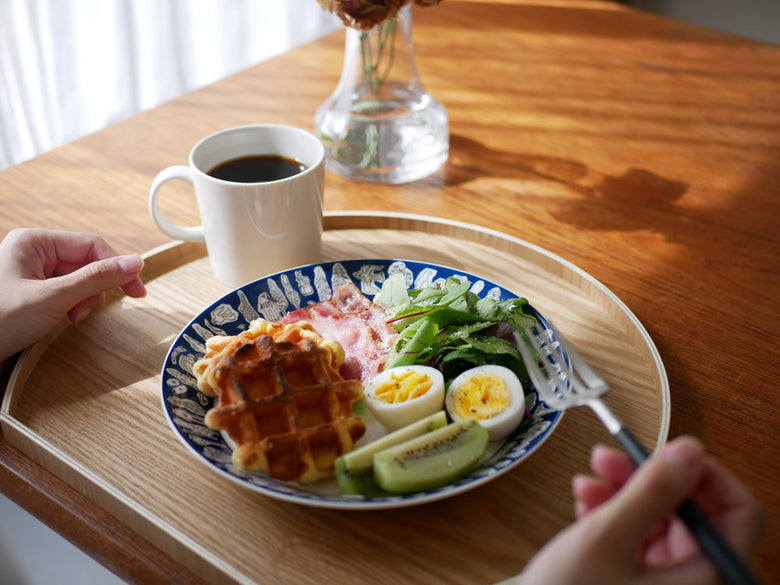 イッタラ×ミナペルホネン フォレストライフ限定カラーの磁器マグカップ、ボウル、プレートが果物とともに朝食テーブルに配置されている様子