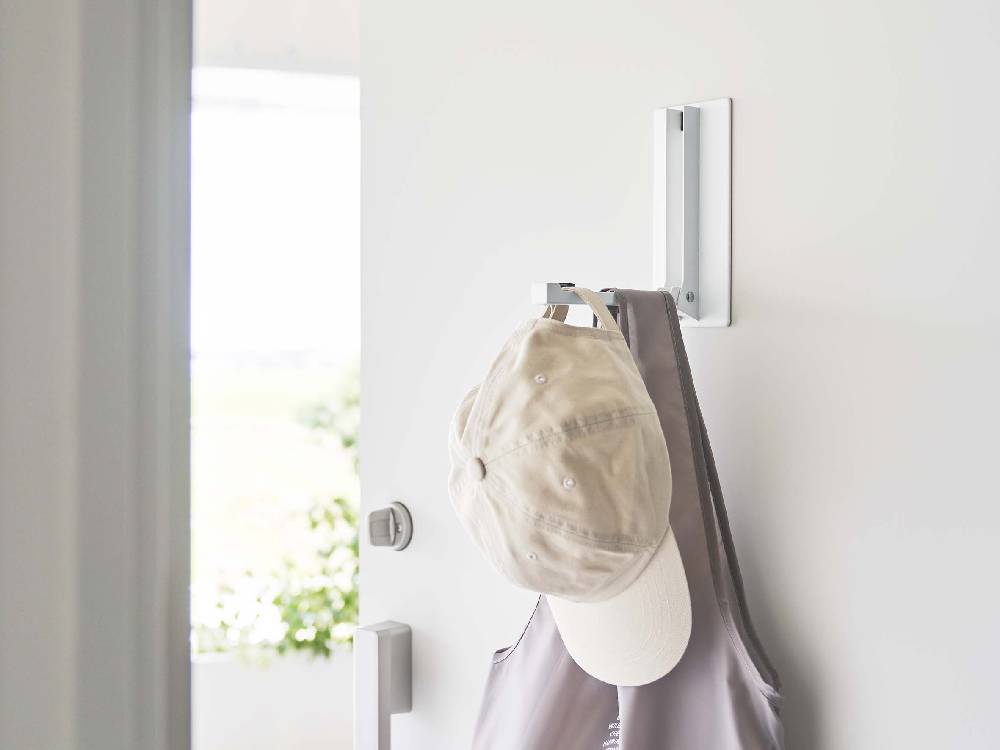 白色のマグネット折りたたみハンガーが壁に取り付けられ、タオルや衣類を掛けている様子
